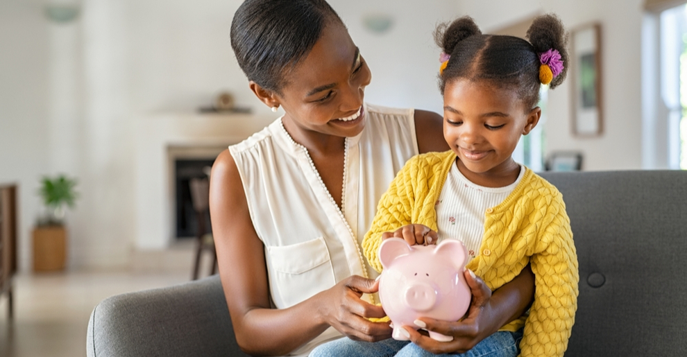 Mother helping young daughter put coins in piggy bank